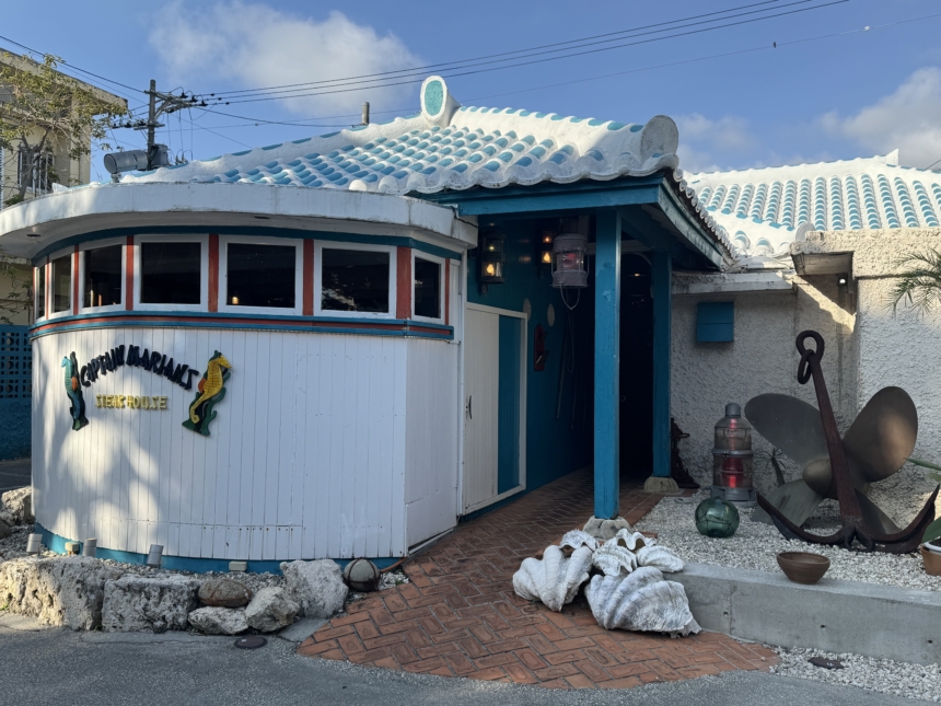 Seafront restaurant with a curved white exterior, turquoise trim, and a blue tiled roof, sea-themed decor on the façade.