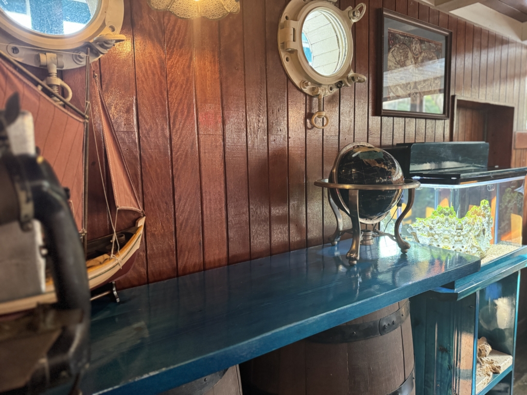 Nautical interior: wood-paneled wall with round porthole windows, a globe on a stand, a framed map, and a blue shelf along the counter.